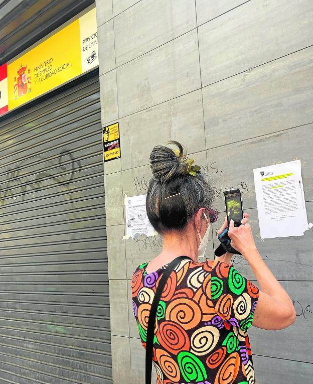 Una mujer saca a una foto a un documento informativo en la fachada de una oficina de empleo. / EUROPA PRESS