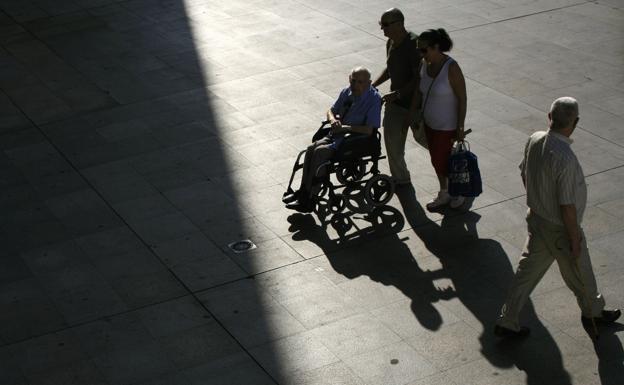 Un pareja empuja la silla de ruedas de un familiar por una calle de Sevilla.