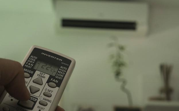A person controls the temperature of the air conditioning with the remote control.