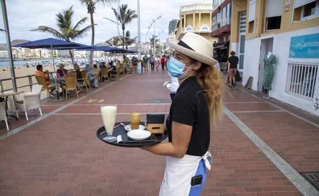 Una camarera atiende a la clientela del local en el que trabaja en la playa de Las Canteras. 