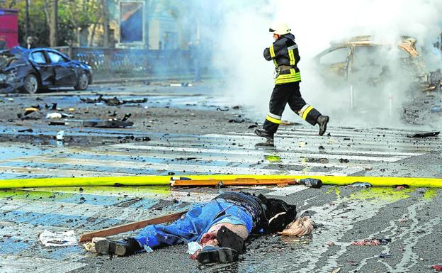 Un bombero pasa corriendo junto al cadáver de una víctima que yace sobre el asfalto tras la explosión de un misil en una calle de Kiev. 