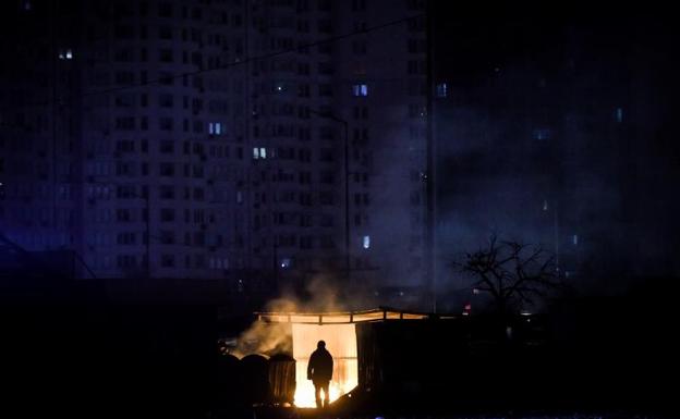Un hombre se calienta en una hoguera junto a un edificio sin suministro eléctrico en Kiev. /EFE